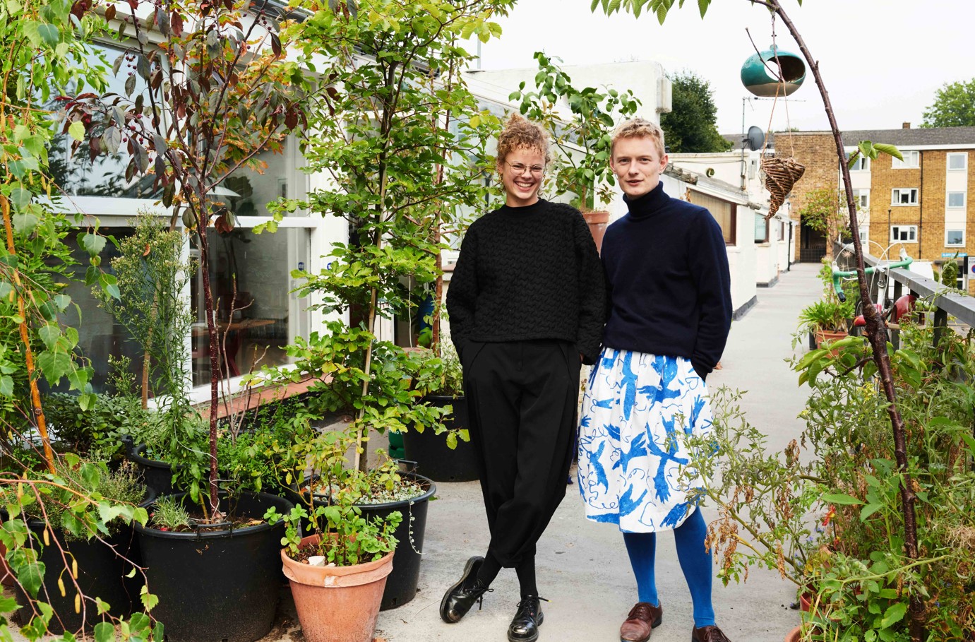 Two people stood outside on a terrace, surrounded by plants
