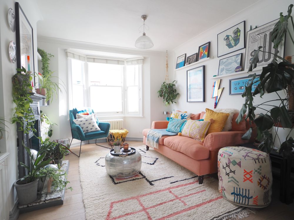 A lounge area with bay windows, pink sofa, pictures on the walls