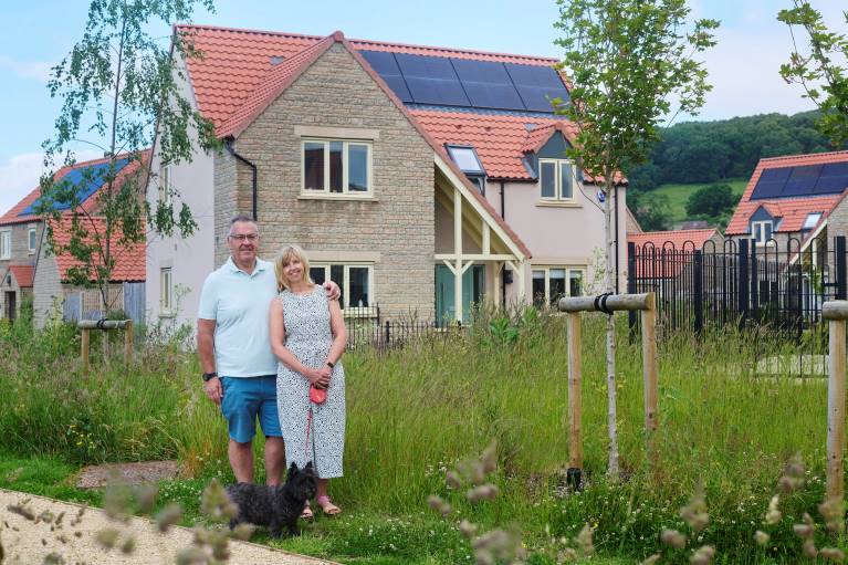 A couple and a dog standing in front of a house