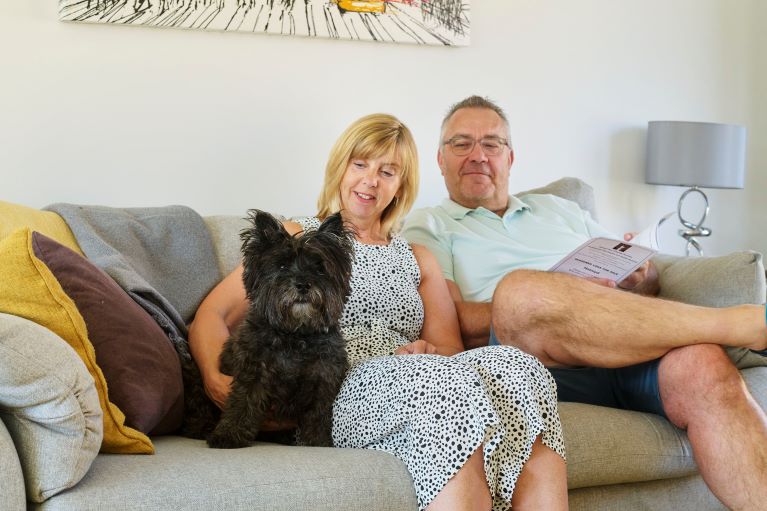 Two people sitting on a sofa with a dog