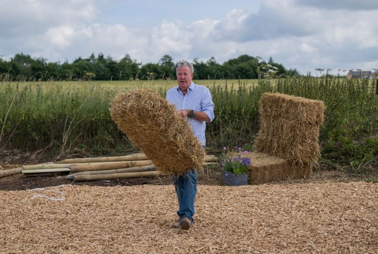 A person in a field carrying a hay bail