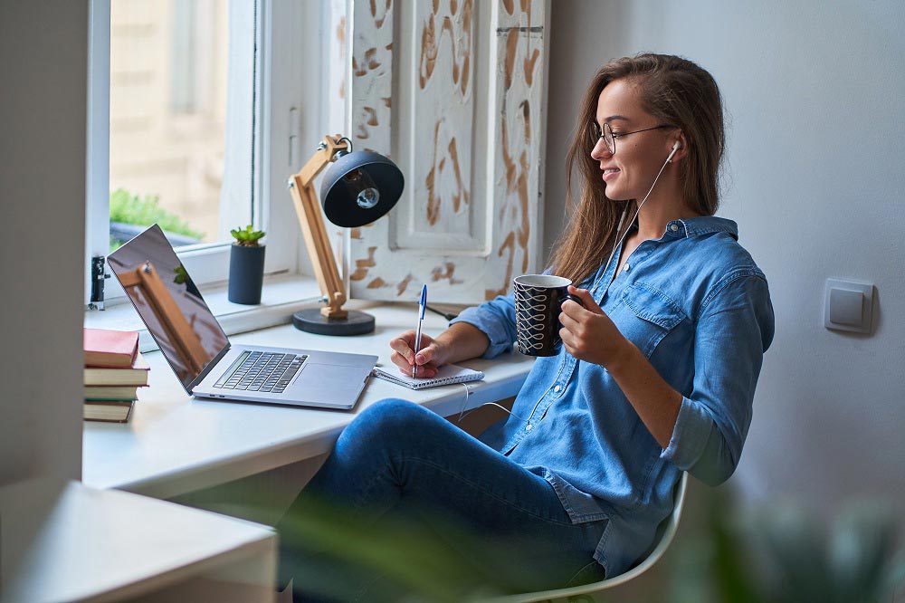 A woman sat at a desk with a laptop, wearing headphones