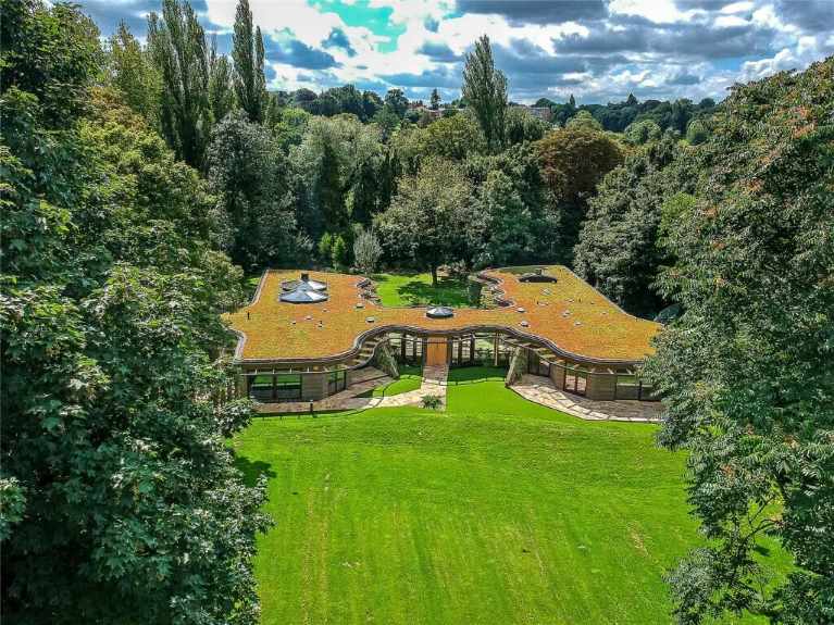 An aerial view of a single storey home with a grass roof, trees, a lawn
