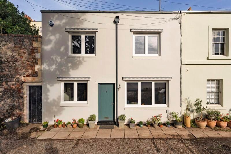 A grey house with a green front door, plant pots