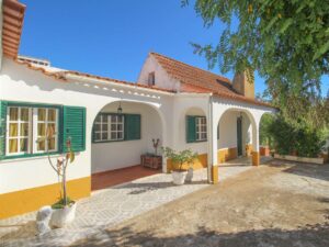 The exterior of a white farmhouse with green shutters and alcove details